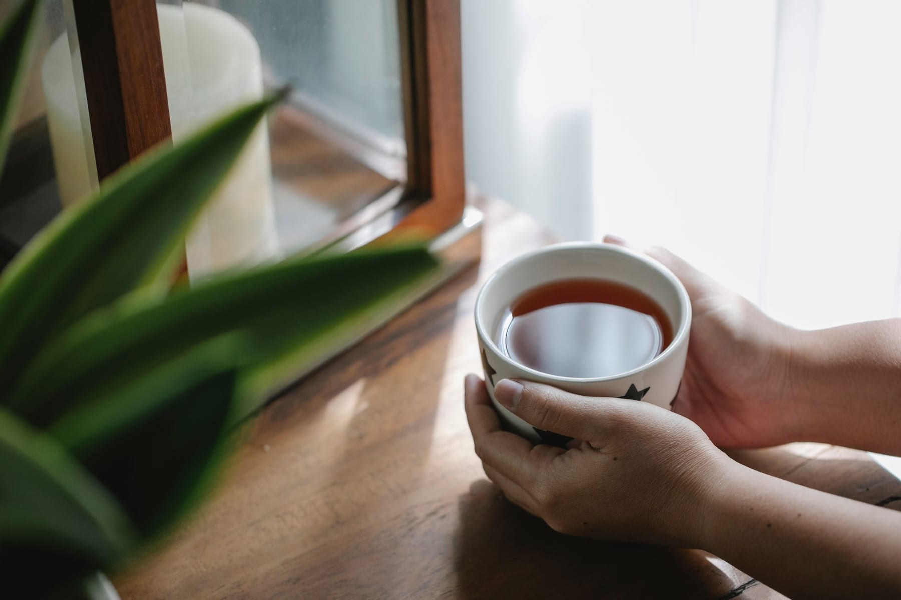 Des mains autour d'une tasse, près de la fenêtre